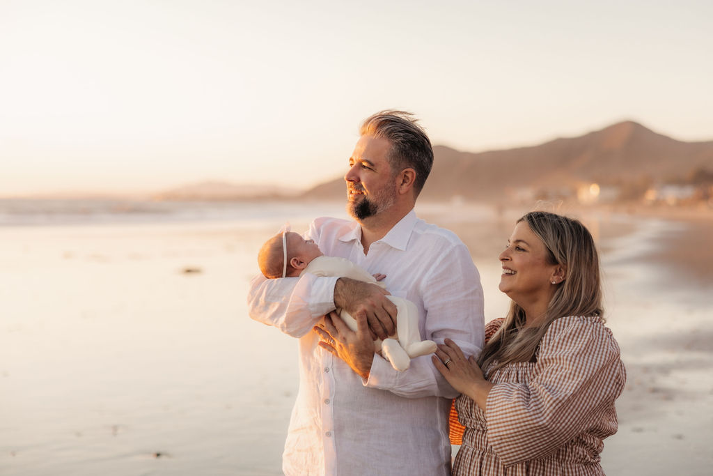 Parents and newborn daughter soaking in the gentle ocean breeze at sunset